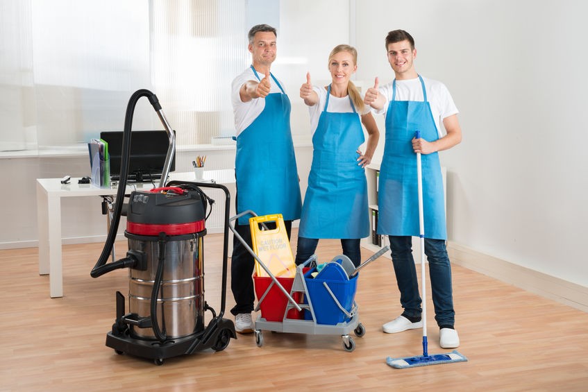 Happy Janitors With Vacuum Cleaner And Cleaning Equipments In Office